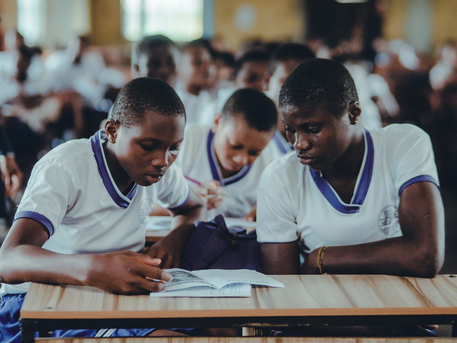 Secondary school students in uniform working at a desk in a school hall